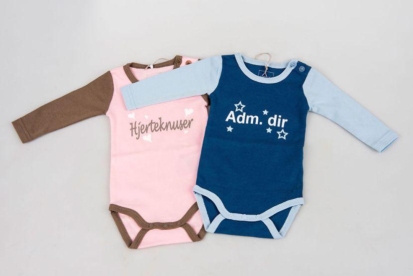 To babybodier, en i rosa med påskriften Hjerteknuser og en i blå med påskriften Adm. dir.